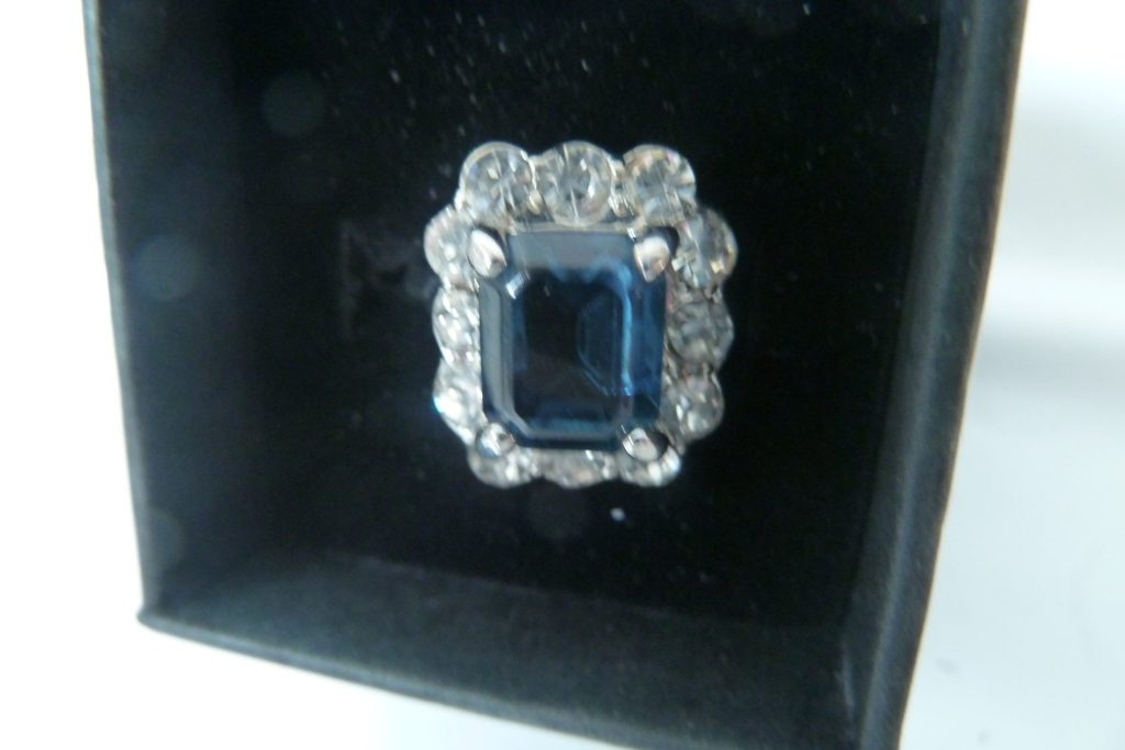 Vintage silver-tone cocktail ring with large emerald-cut dark blue gemstone surrounded by clear rhinestones in a black velvet box