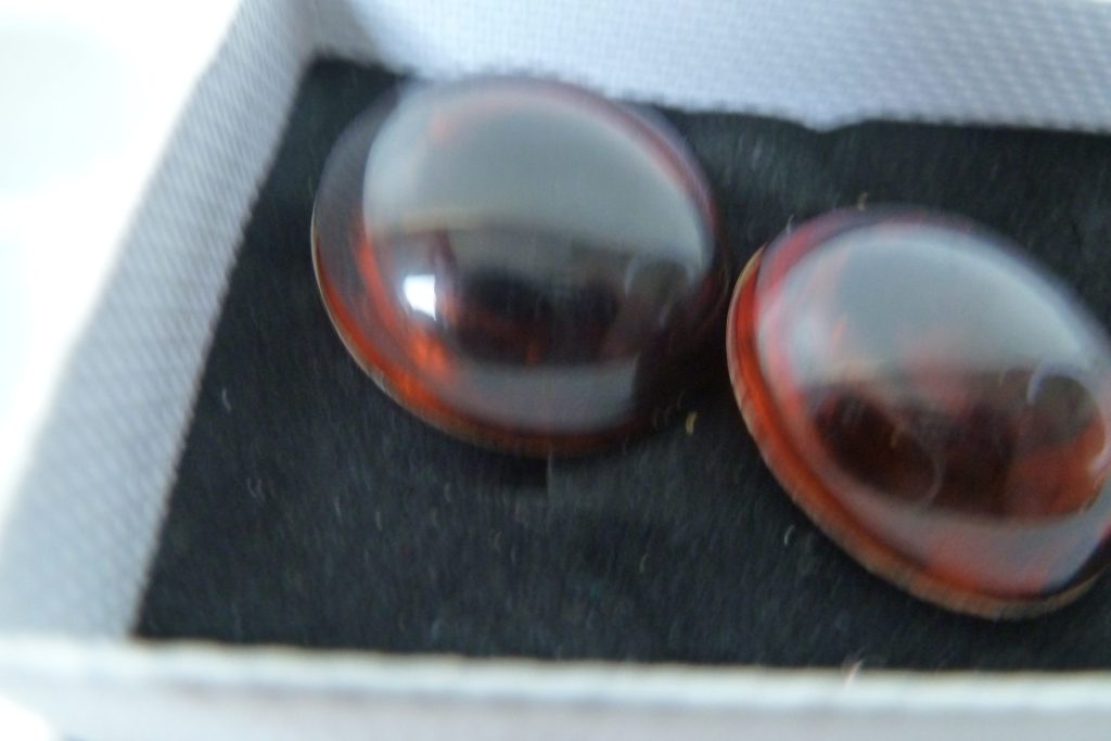Two domed, reddish-brown resin or amber cabochons in a gray and black jewelry box