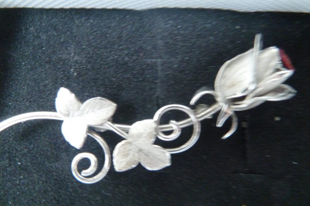 Silver-tone floral brooch with rosebud and leaves on a dark background